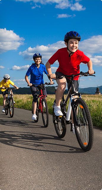 Three children joyfully riding bicycles along a scenic road, showcasing their enthusiasm for outdoor activities.
