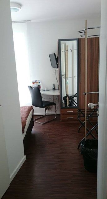 Eine Seitenansicht eines Hotelzimmers mit einem Bett, Schreibtisch und Stuhl, die einen gemütlichen und funktionalen Raum für Gäste zeigt.
